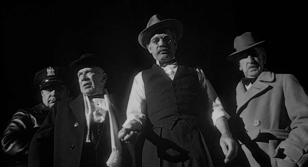 Touch of Evil (1958) movie still: medium — Four men stand close together in a pitch-black environment under stark upward illumination. They appear…