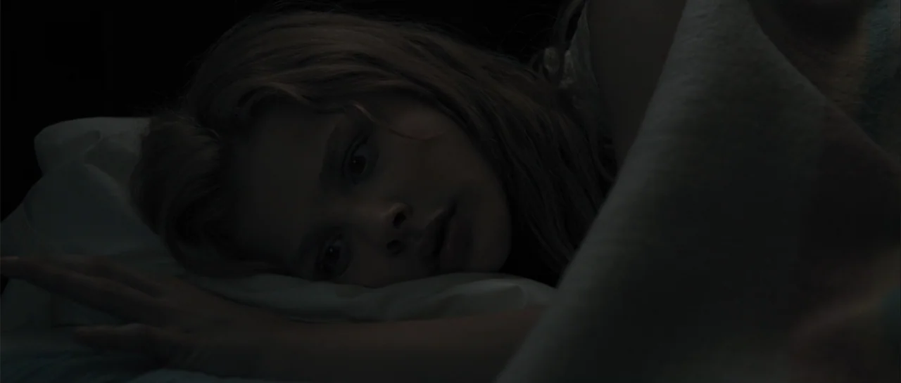 Carrie (2013) movie still: closeup — A dark, dimly lit bedroom at night with a woman lying in bed. The subject rests her head on a pillow while…