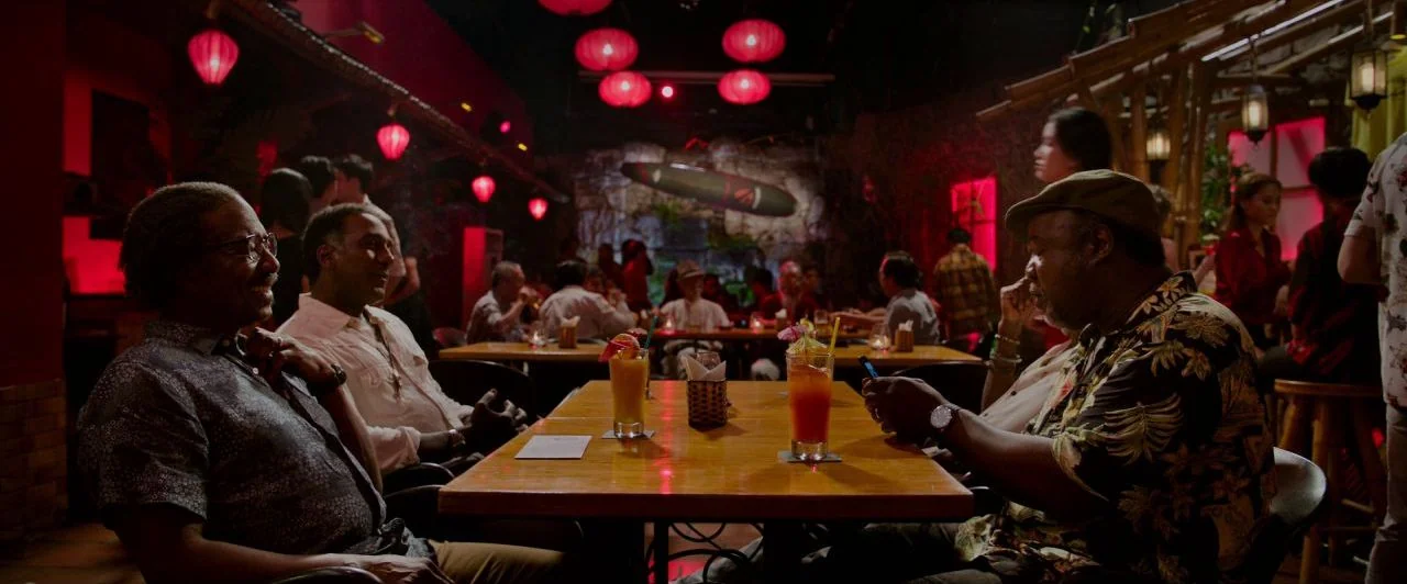 Da 5 Bloods (2020) movie still: medium — A dimly lit bar space filled with red paper lanterns and wooden furniture features. Several men sit around…