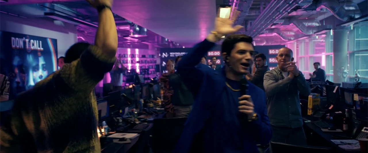 The Beekeeper (2024) movie still: medium — A busy open-plan office space is illuminated by vibrant magenta neon lighting fixtures. A man in a blue…