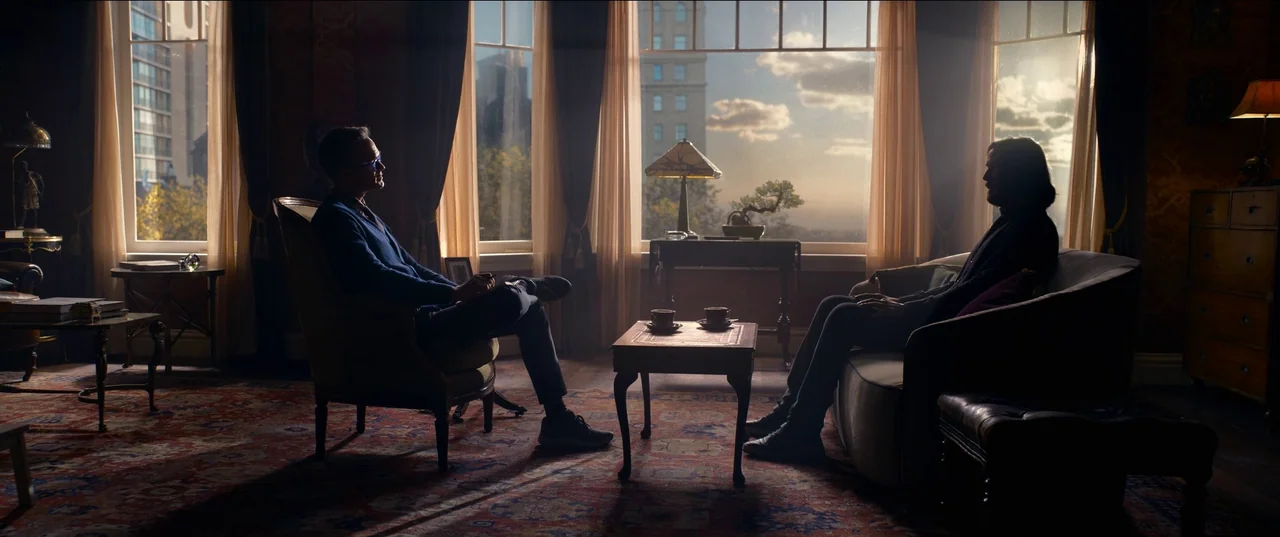 The Matrix Resurrections (2021) movie still: wide — An opulent room with floor-to-ceiling windows looking out onto a modern city skyline. Two men…