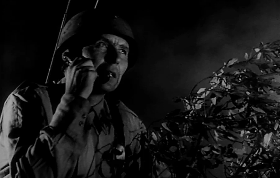 Caltiki, The Immortal Monster (1959) movie still: medium — A nighttime outdoor setting featuring a soldier positioned behind thick, dark foliage.…