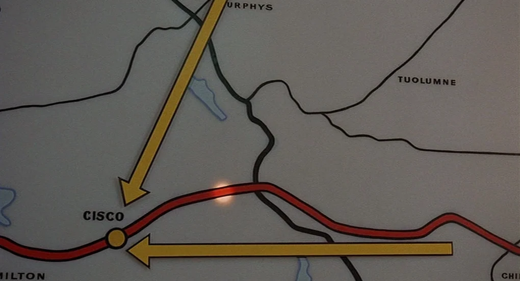 Vanishing Point (1971) movie still: closeup — A close-up view of a printed wall map showing various town names and roads. Bright yellow arrows point…