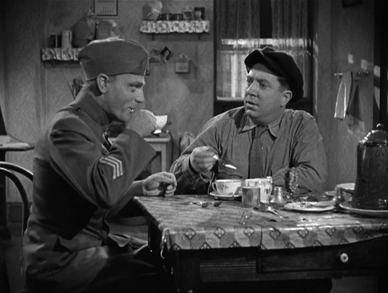 The Roaring Twenties (1939) movie still: medium — A modestly furnished room with a checkered tablecloth and sparse wall decorations. Two men in…