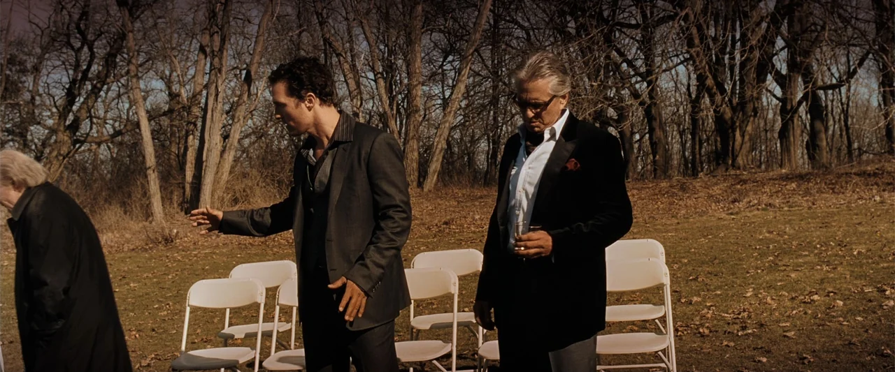 Ghosts of Girlfriends Past (2009) movie still: medium — Two men in formal attire stand in a dry, grassy clearing lined with folding chairs. The…