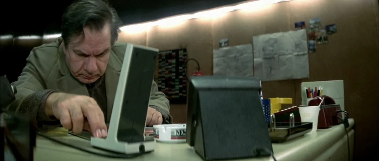 Subway (1985) movie still: medium — A workspace features wood-paneled walls decorated with scattered papers and a small desk lamp. A middle-aged man…