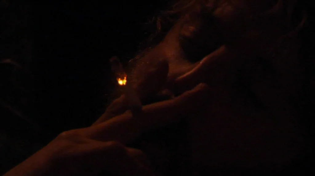 Humpday (2009) movie still: closeup — A person stands in a completely dark space with almost no visible background. Their hand holds a burning…
