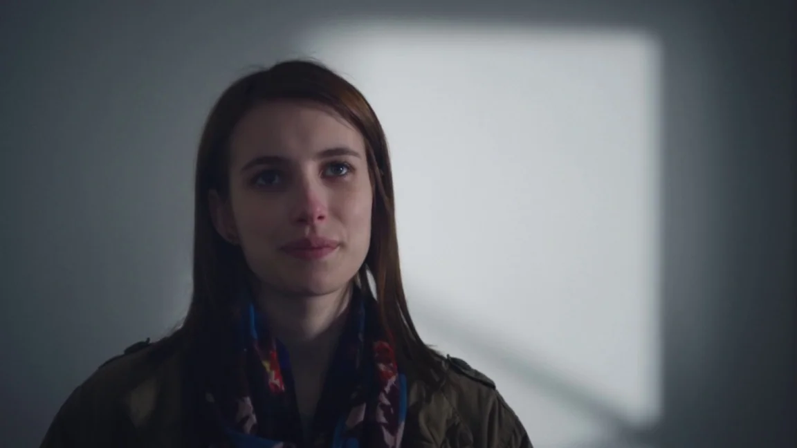 Adult World (2013) movie still: closeup — A sparsely furnished room features a plain gray wall with a window light beam. A young woman with brown…
