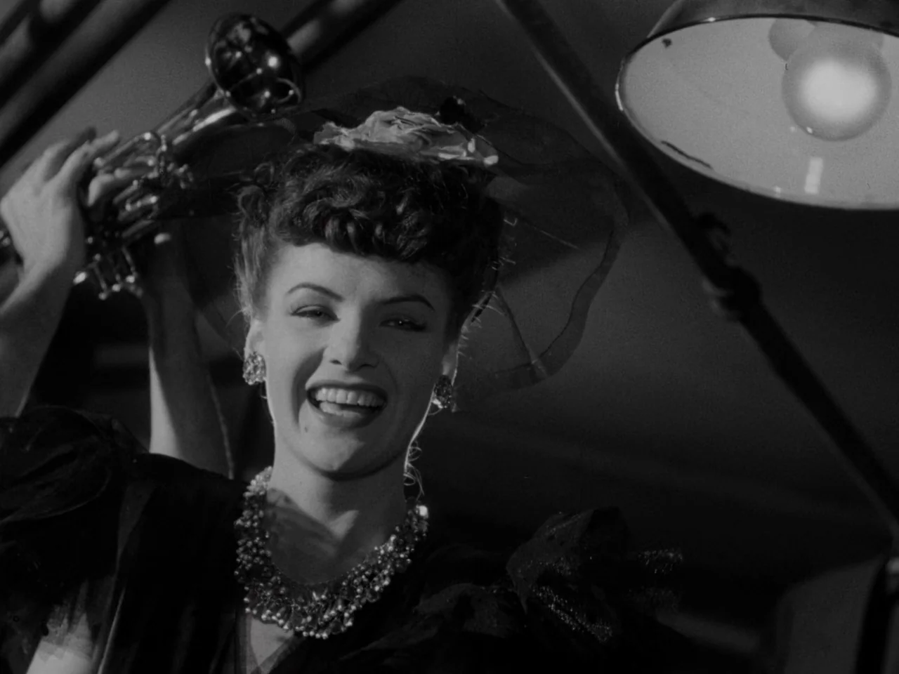 Phantom Lady (1944) movie still: closeup — A dark, dimly lit environment features a woman in formal 1940s evening attire. She holds a brass trumpet…