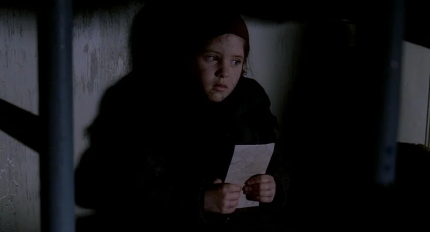 The Man Who Cried (2000) movie still: medium — A dark, cramped interior space features vertical metal poles and a plain wall. A young girl sits…