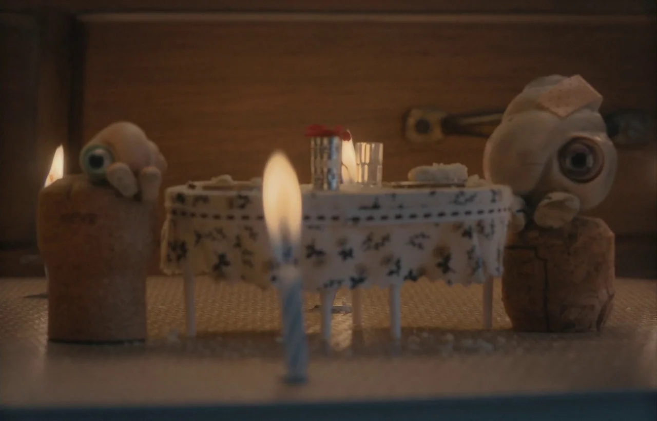 Marcel the Shell with Shoes On (2021) movie still: medium — Two small creatures constructed from shells and cork sit at a miniature table. A small…