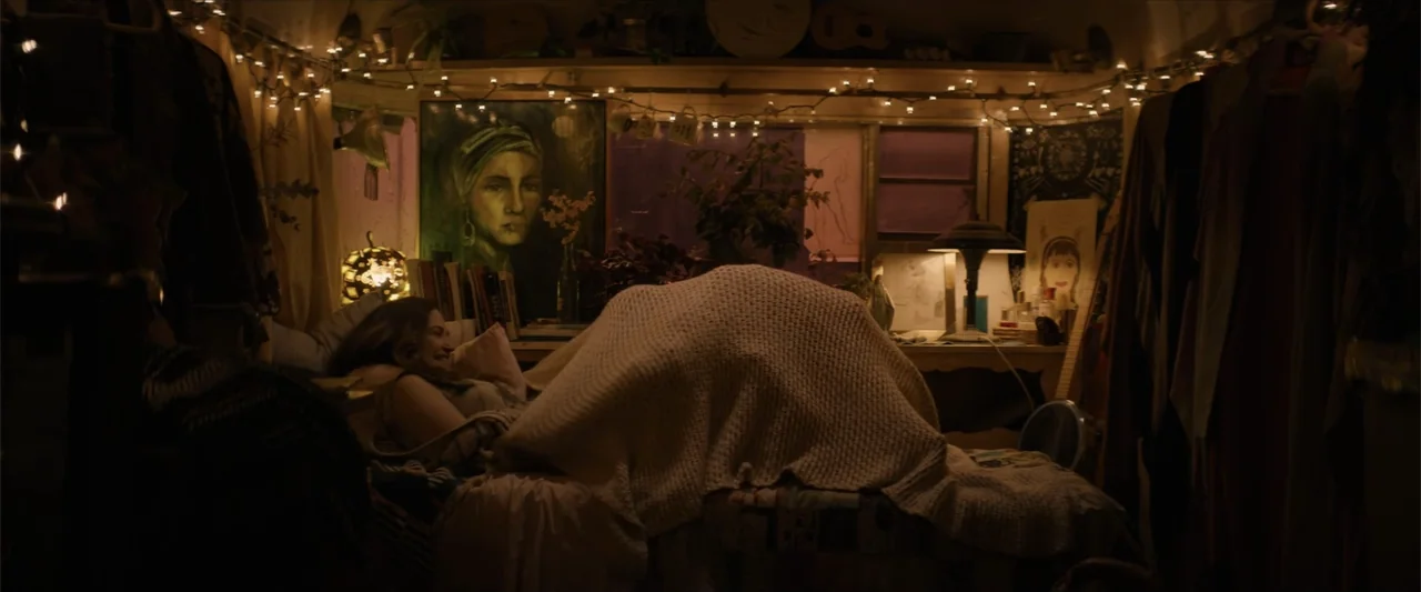 Equation of Love and Tone Deafness (2015) movie still: medium — The interior of a small, cluttered camper is decorated with paintings and string…