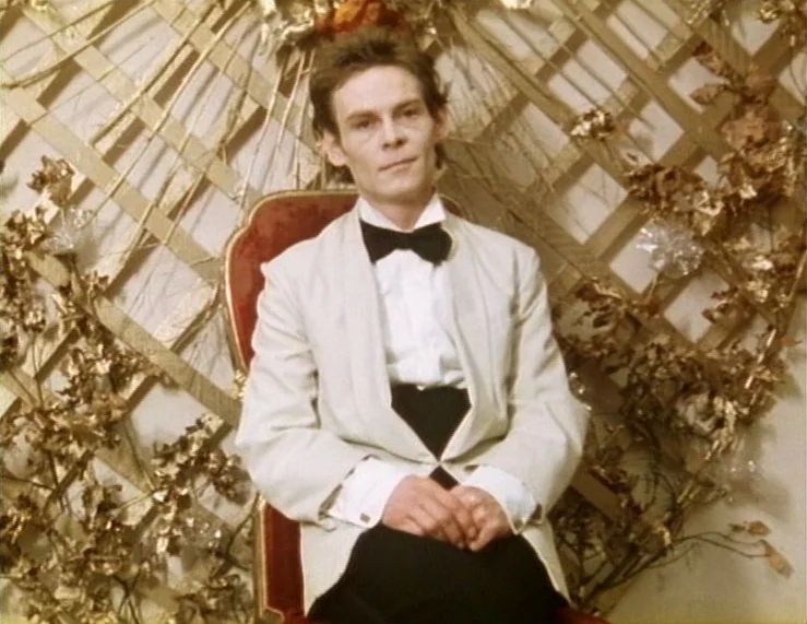 The Tempest (1979) movie still: medium — A person sits before a lattice screen adorned with gilded dried leaves and flowers. The subject wears a…