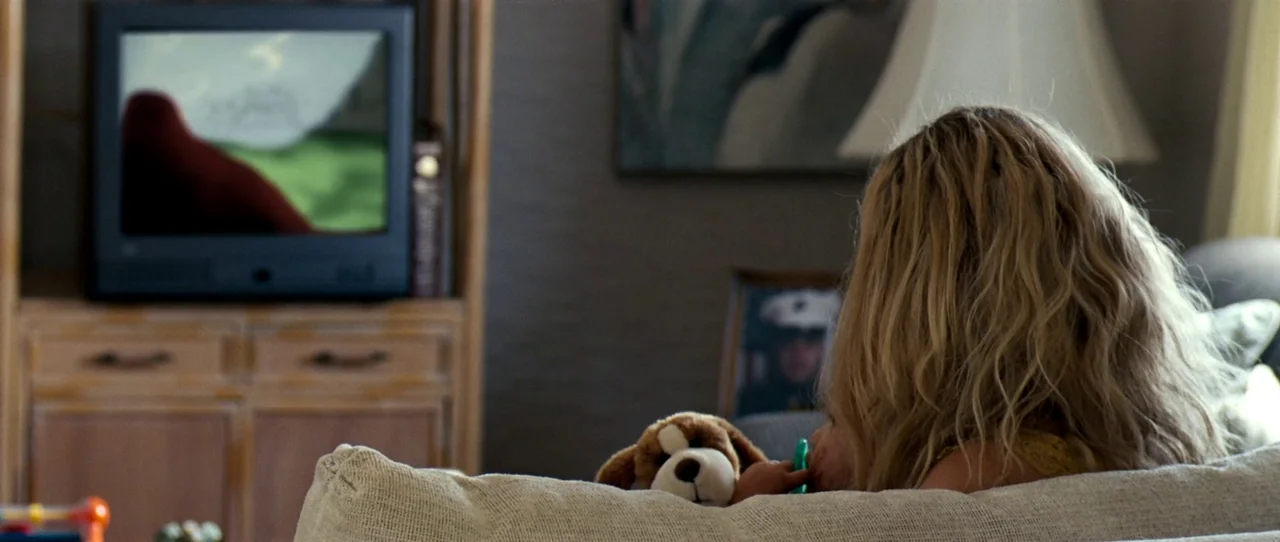 Little Birds (2011) movie still: medium — A living room features an entertainment center with a television and a framed photograph. A child with…