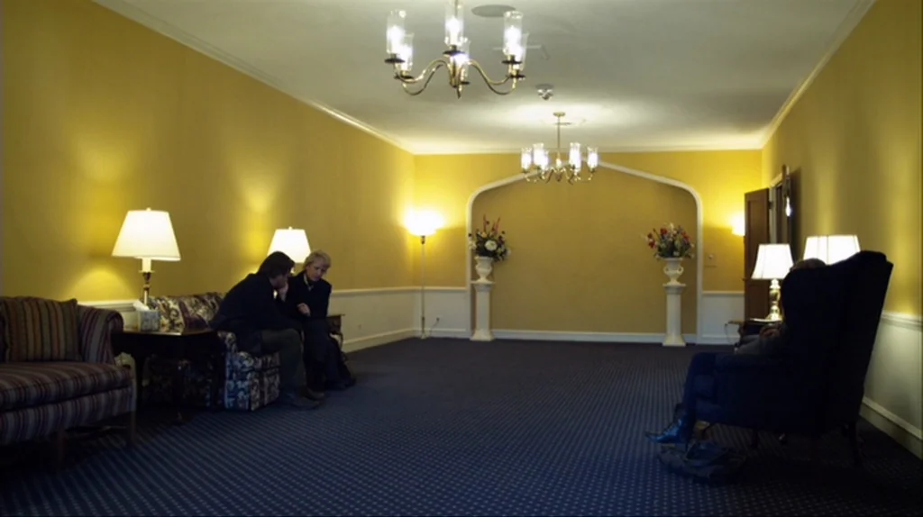 Contagion (2011) movie still: wide — A spacious, yellow-walled waiting room features dark blue carpeting and multiple ornate chandeliers overhead.…