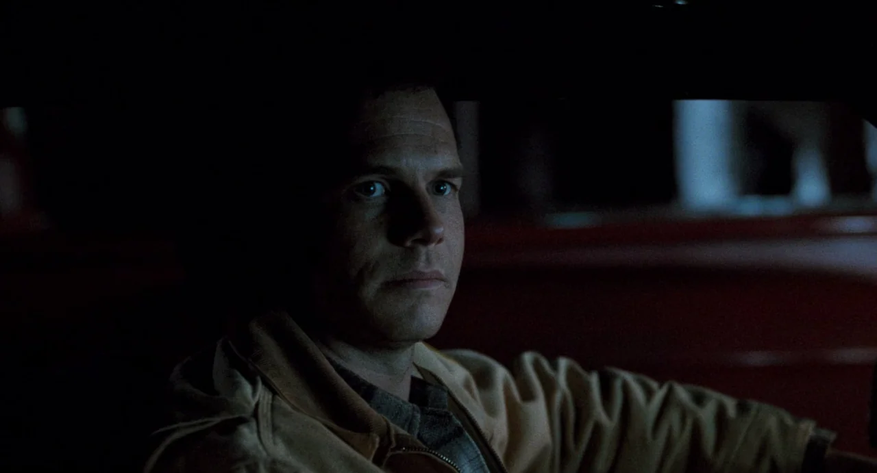 One False Move (1991) movie still: closeup — A dark vehicle cabin at night with minimal ambient lighting. A man sits in the driver's seat looking…