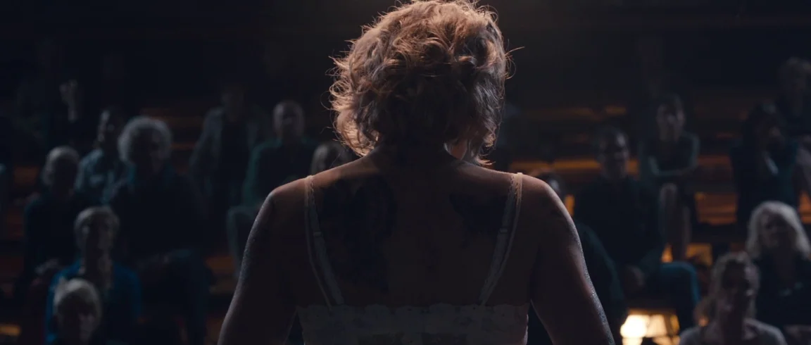 Broken Circle Breakdown (2012) movie still: medium — A woman stands in the foreground facing a dark, crowded room filled with spectators. Large dark…