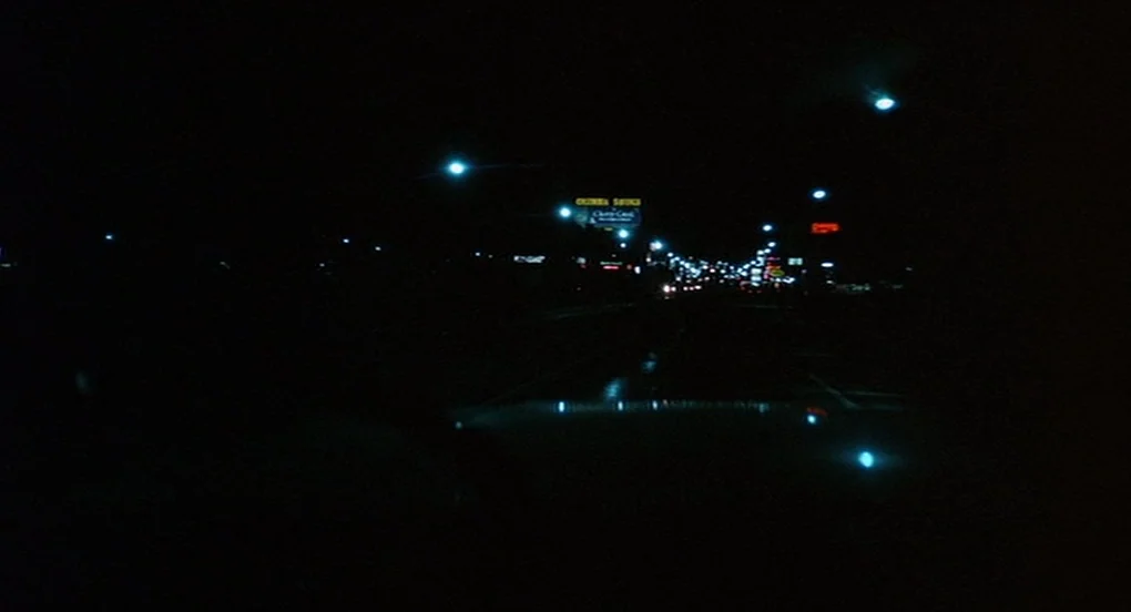 Vanishing Point (1971) movie still: establishing — A dark urban road at night is lit by distant streetlamps and commercial signs. The perspective is…