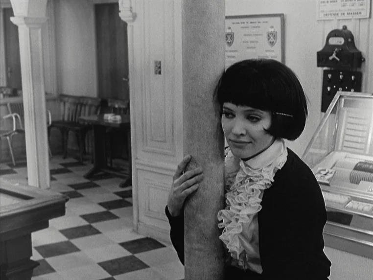 Vivre Sa Vie (1962) movie still: medium — The interior of a cafe features a checkerboard floor and ornate architectural columns. A woman with a…
