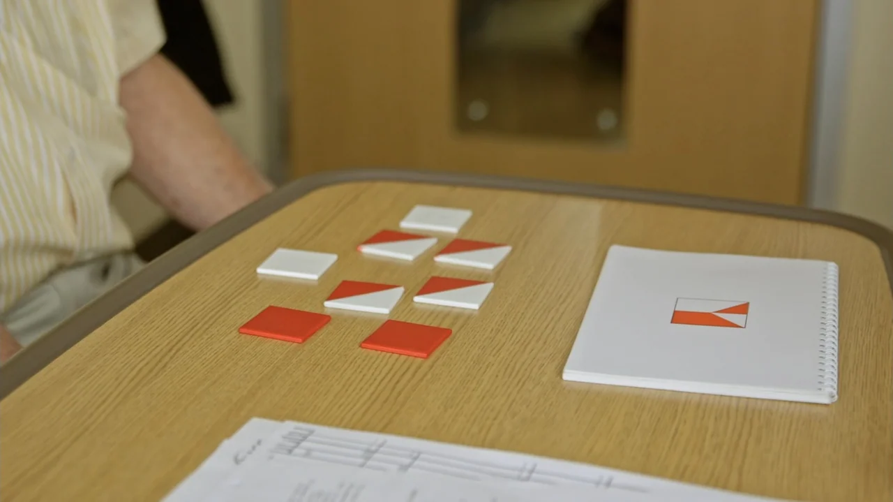Moonlight Sonata: Deafness in Three Movements (2019) movie still: medium — A light wood table in a clinical interior holds a set of geometric tiles.…