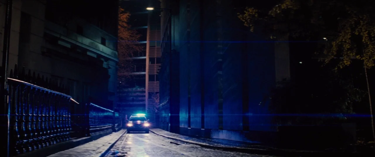 Mission: Impossible – Rogue Nation (2015) movie still: wide — A narrow urban alleyway is flanked by dark brick buildings and an iron fence. A police…