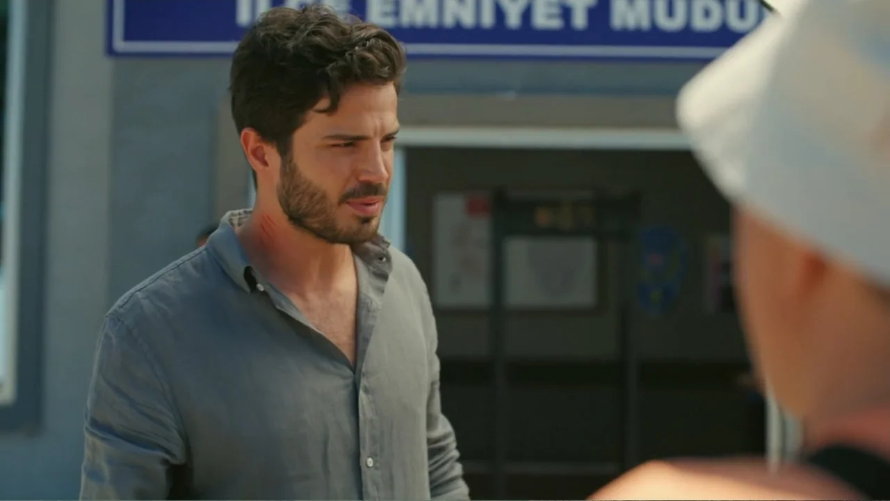 Paranormal Cuma (2024) movie still: medium — An exterior entrance to a police station with a blue sign above the door. A man with a dark beard and a…