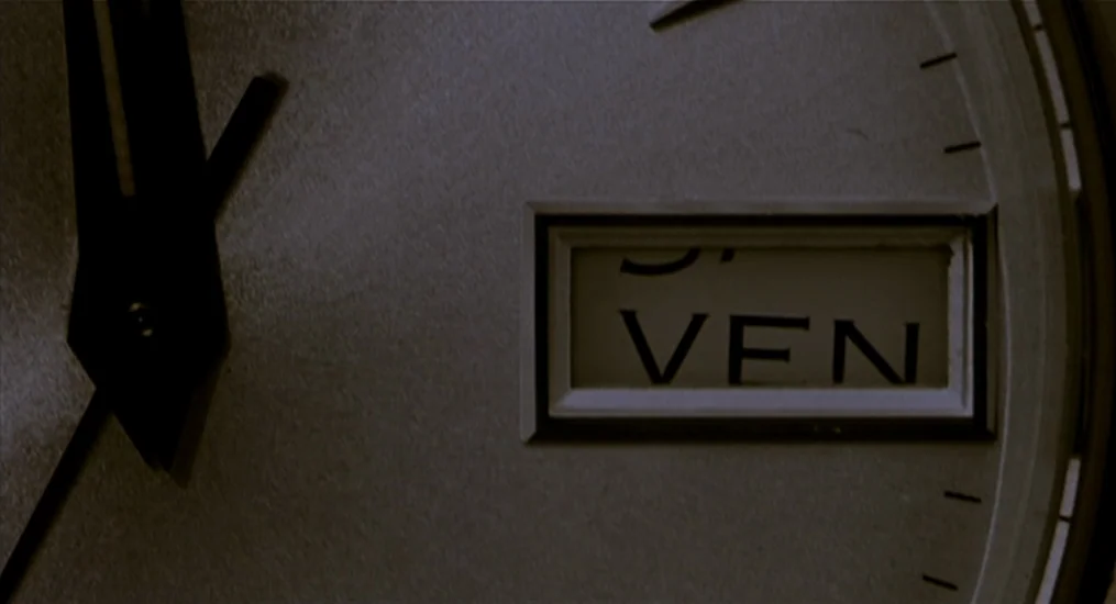 Vendredi Soir (2002) movie still: closeup — A close-up view shows the metallic face of an analog watch. The day display is partially visible with…