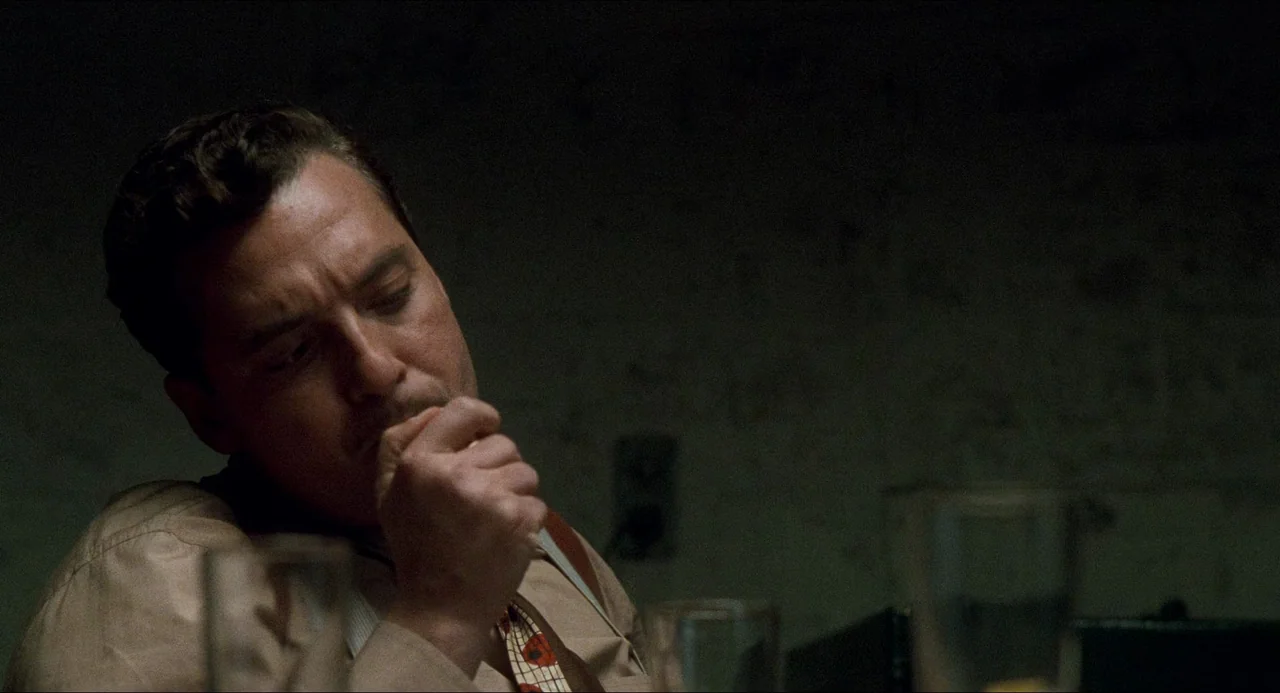 Devil In A Blue Dress (1995) movie still: closeup — A dark, dimly lit interrogation room with a rough, textured wall behind the subject. A man in a…