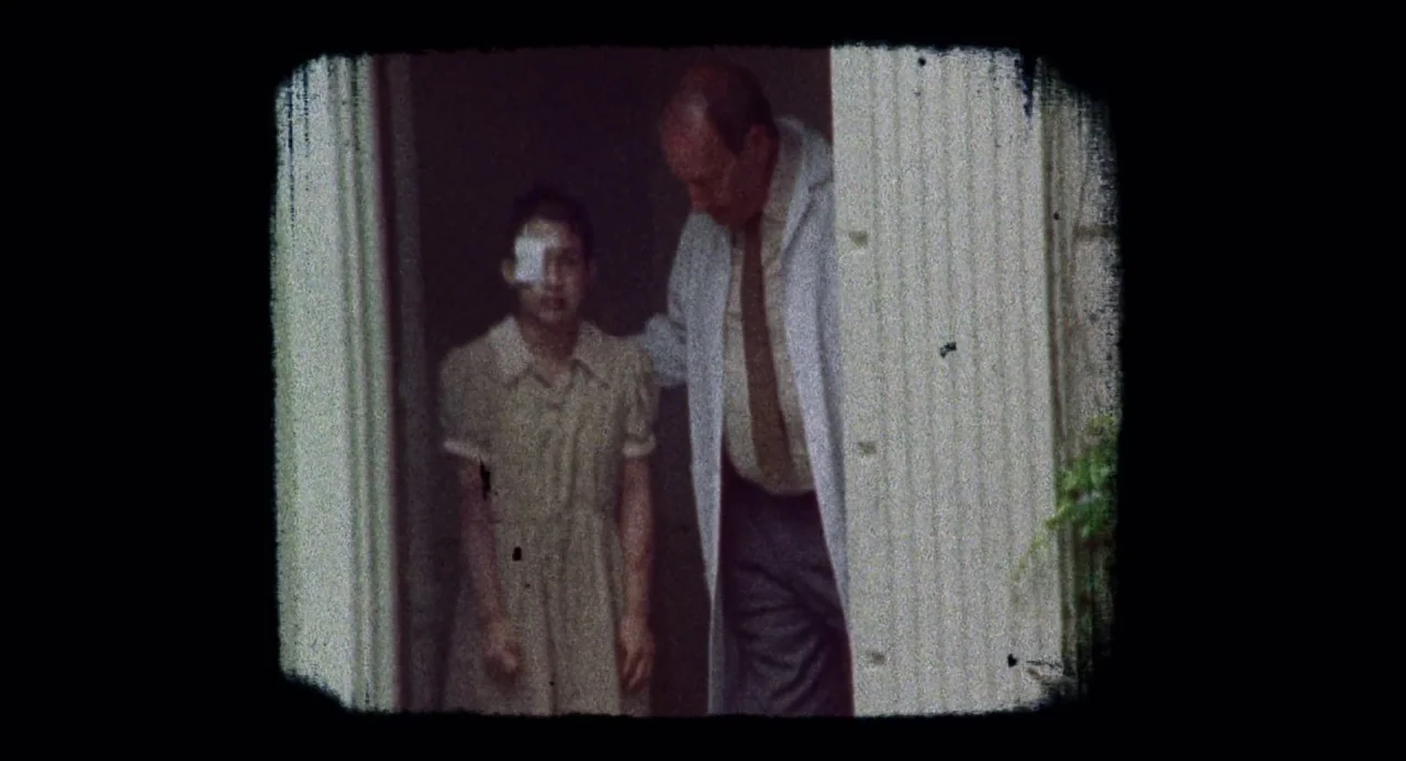 Martyrs (2008) movie still: medium — A man and a girl stand in a doorway of an older building. The girl has an eye patch and the man wears a lab coat.