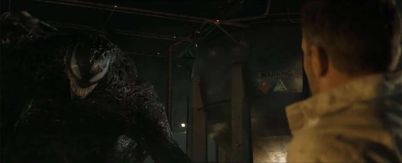 Venom: The Last Dance (2024) movie still: medium — An industrial facility featuring large metal tanks and pipes in the dark background. A large…