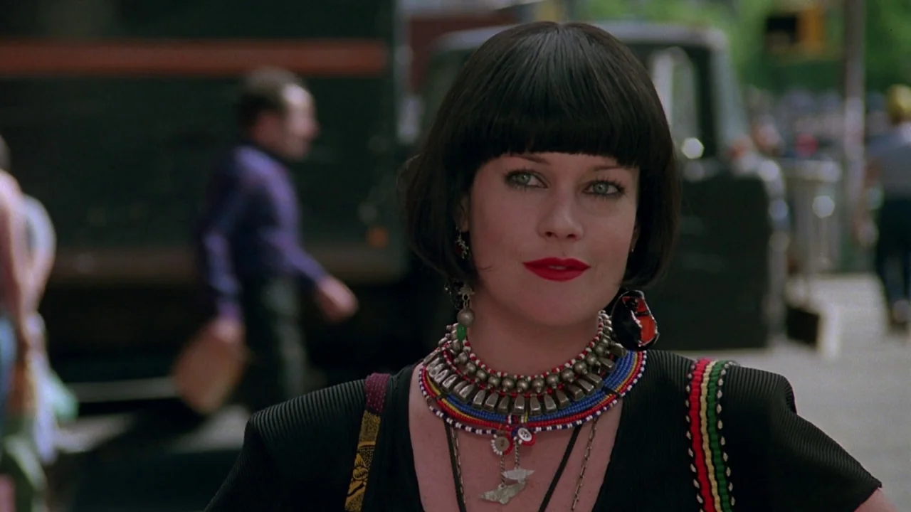 Something Wild (1986) movie still: medium — An outdoor urban sidewalk in the 1990s with blurred city traffic in the background. A woman with a black…