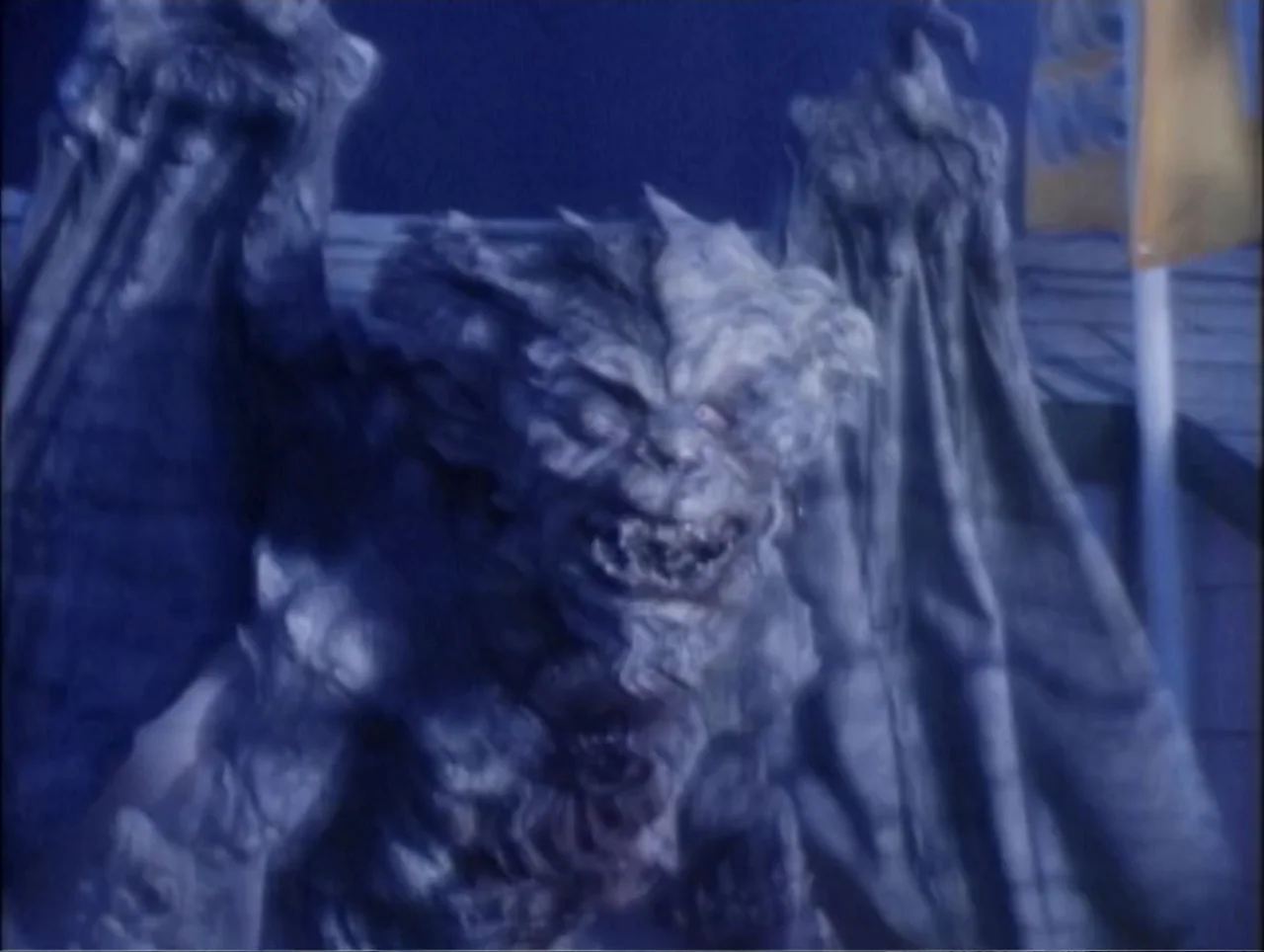 Cast a Deadly Spell (1991) movie still: medium — A stone gargoyle creature with large wings stands atop a building at night. The creature bares its…