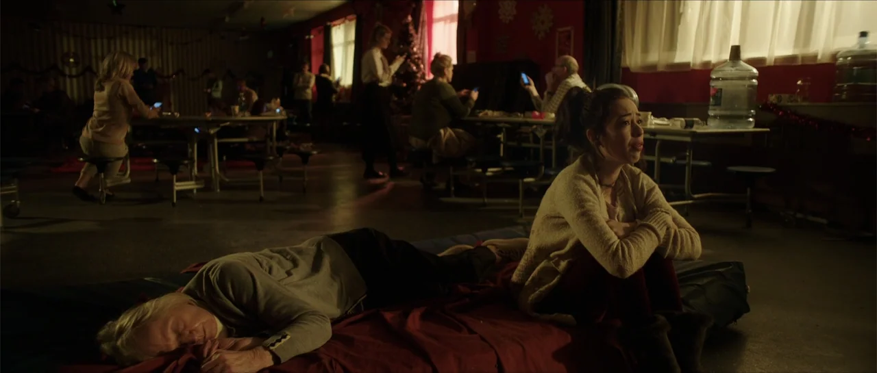Anna and the Apocalypse (2018) movie still: medium — A spacious community center interior with tables and people occupies the background area. In…