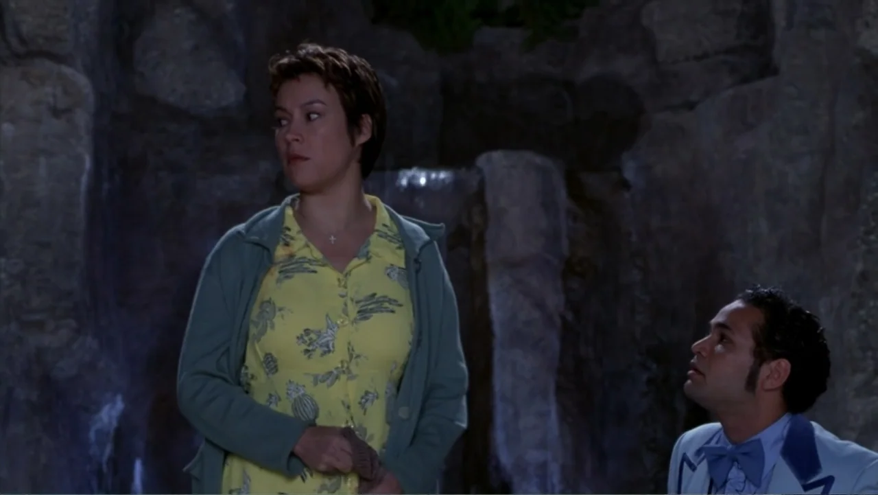 Music from Another Room (1998) movie still: medium — A dark rocky grotto with a small waterfall feature in the background. A woman stands in front…