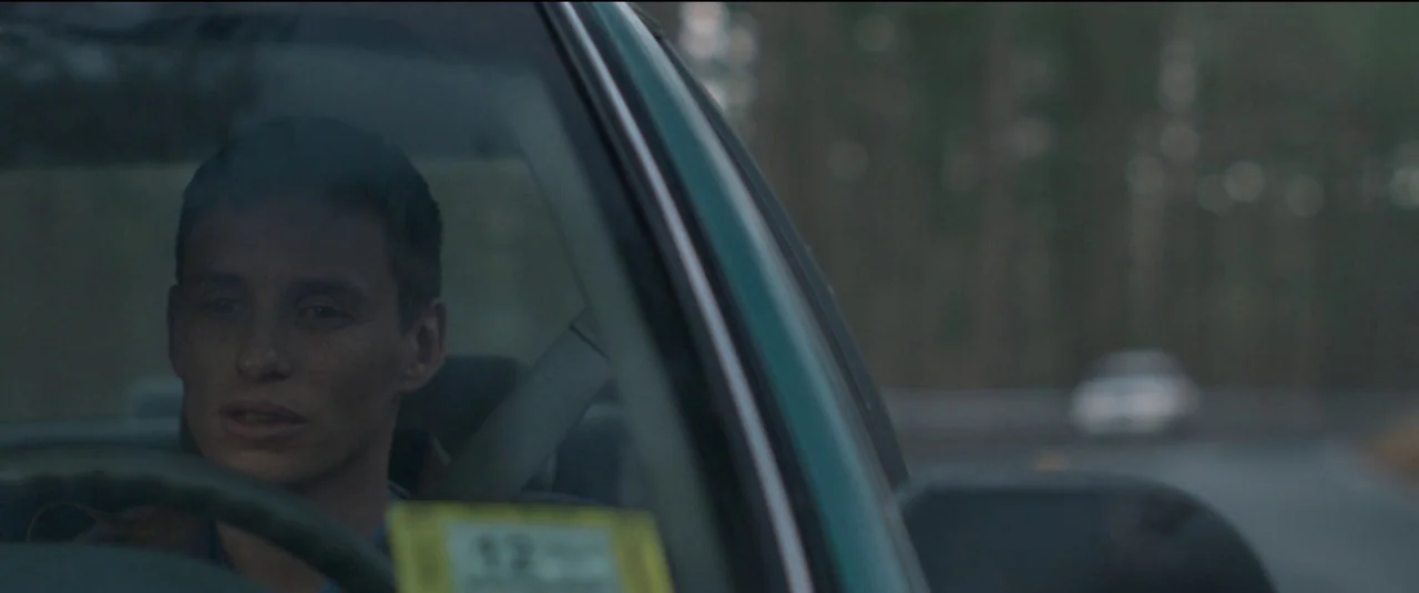 The Good Nurse (2022) movie still: medium — A man sits inside a vehicle with a forest blurred in the background. The man operates the steering wheel…