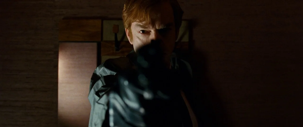 Cloud Atlas (2012) movie still: closeup — A dimly lit room with textured dark wallpaper serves as the backdrop for a confrontation. A man looks…