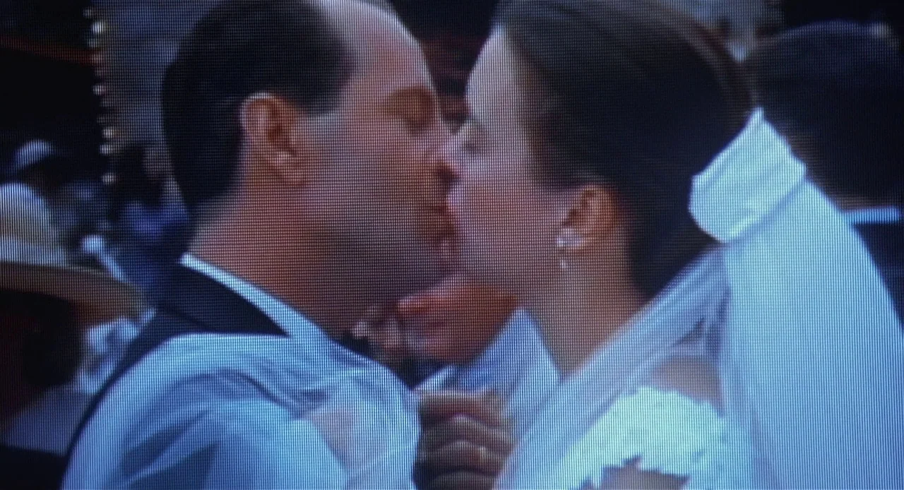 The Sixth Sense (1999) movie still: closeup — A close-up view depicts a man and a woman in formal wedding attire. The couple embraces and kisses…