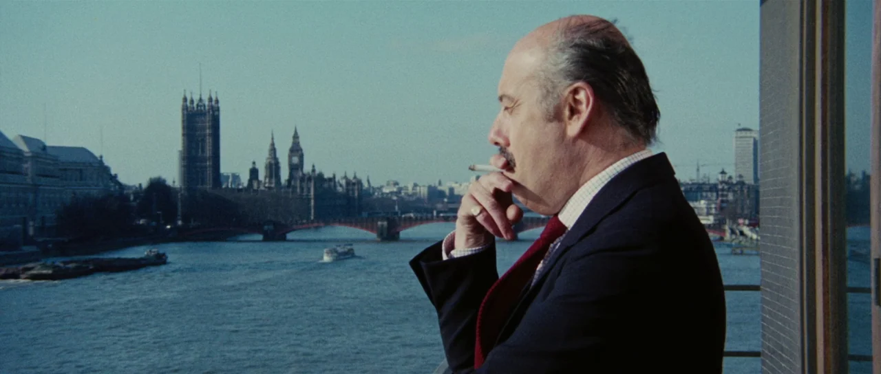 Death Walks On High Heels (1971) movie still: medium — A view of the River Thames and the Houses of Parliament from a balcony. A middle-aged man…