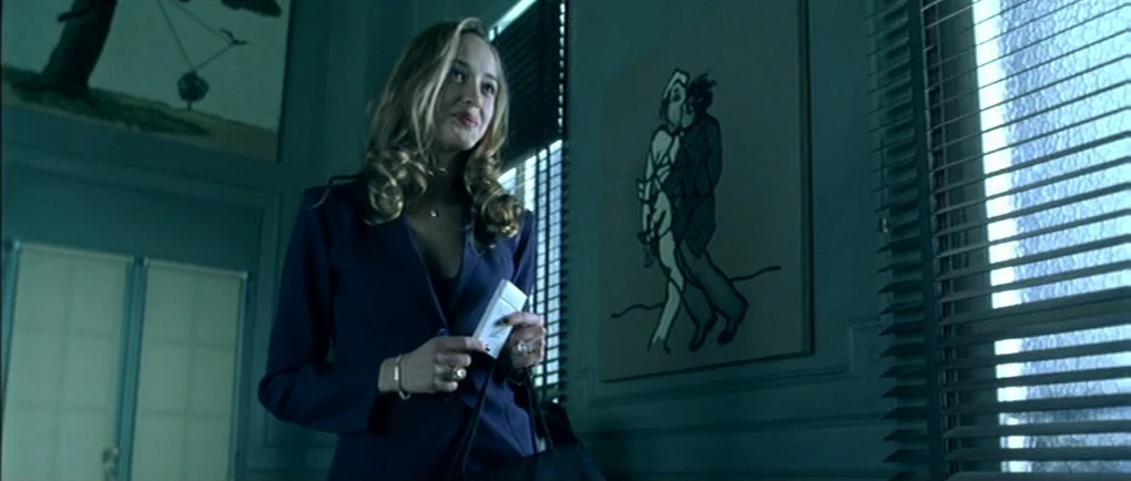Mortal Transfer (2001) movie still: medium — A room with teal-toned walls features framed artwork and large windows with horizontal blinds. A young…