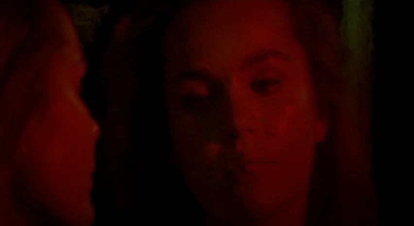 A Safe Place (1971) movie still: closeup — A very dark interior environment with minimal light detail aside from the subjects faces. Two women stand…
