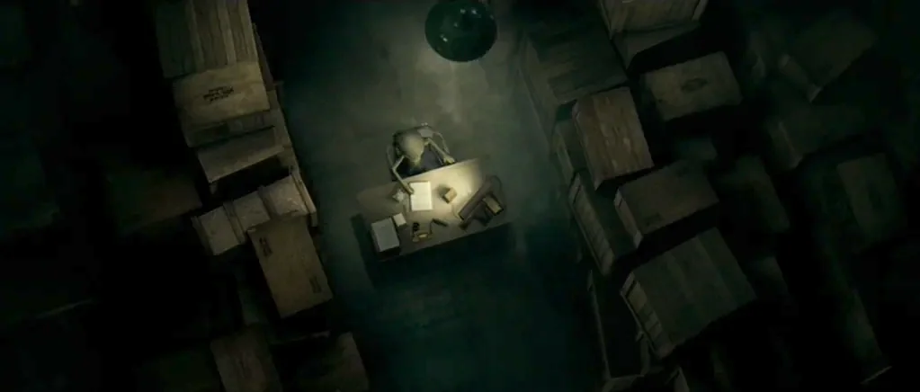 Paul (2011) movie still: wide — A dark, cramped storage room filled with stacks of wooden crates in the shadows. A slender figure sits at a small…