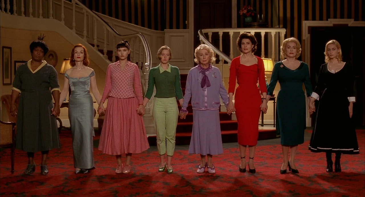 8 Women (2002) movie still: fullbody — A grand foyer with a curved white staircase features eight women standing in line. They face the camera while…