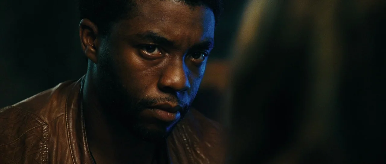 Message From The King (2016) movie still: closeup — A man stands in a dark environment with indistinct features in the background. The man gazes…