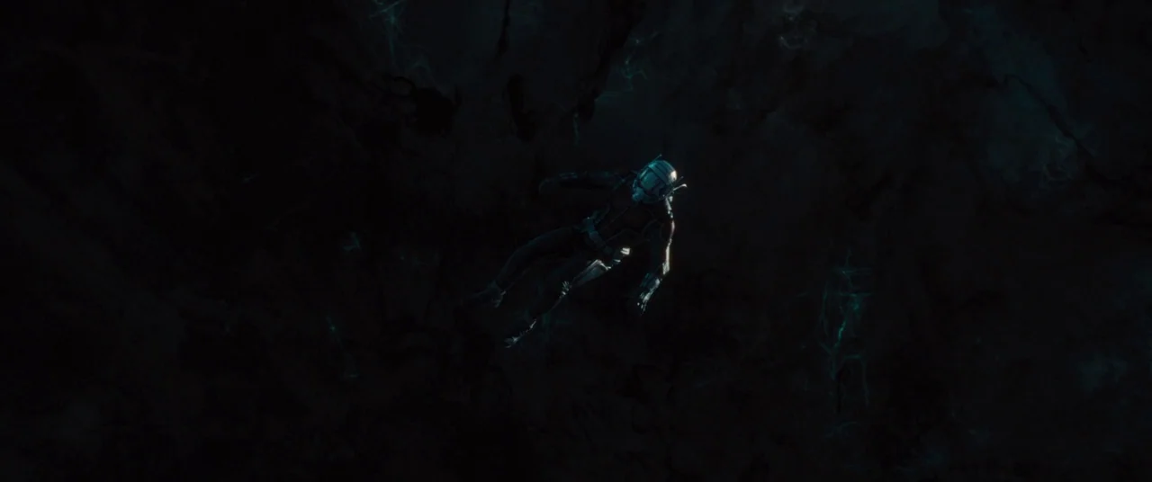 Ant-Man and the Wasp (2018) movie still: wide — A dark, expansive space filled with faint cyan glowing nebulous structures. A single armored figure…