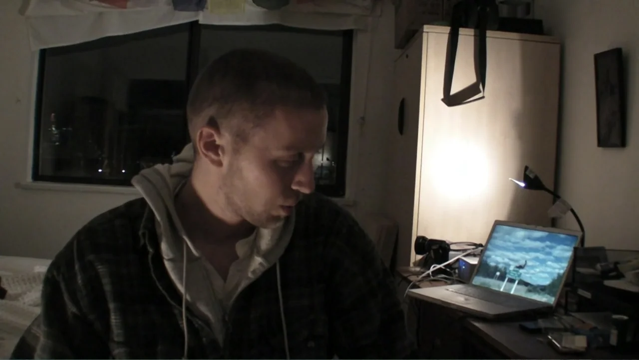 Daniel (1983) movie still: medium — A dimly lit bedroom features a desk against the wall with a glowing laptop screen. A young man sits in front of…
