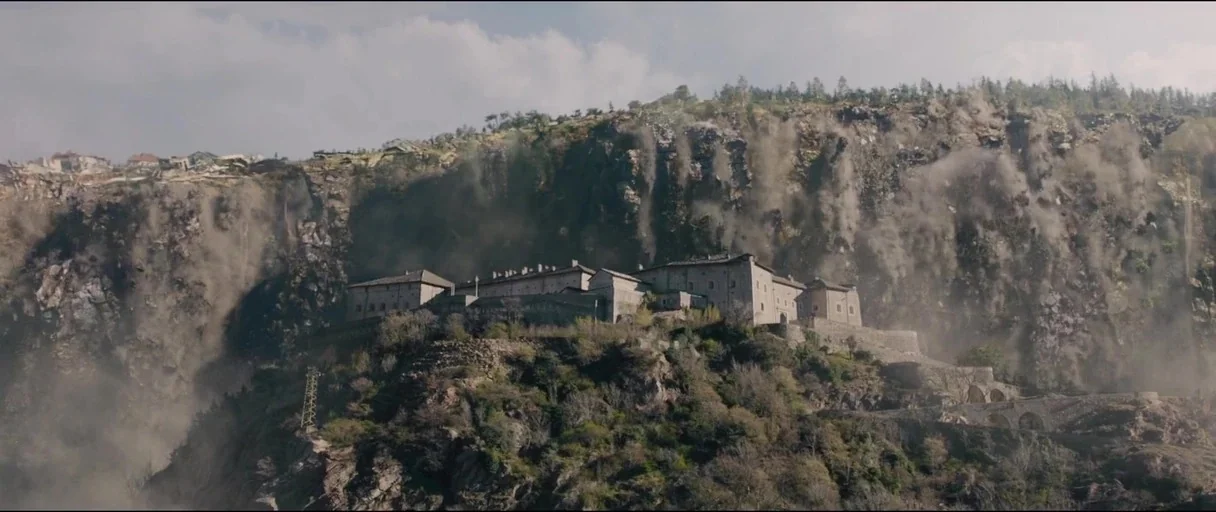 Avengers: Age of Ultron (2015) movie still: establishing — A stone complex sits on a rocky mountain ridge during a landslide event. Dust cascades…