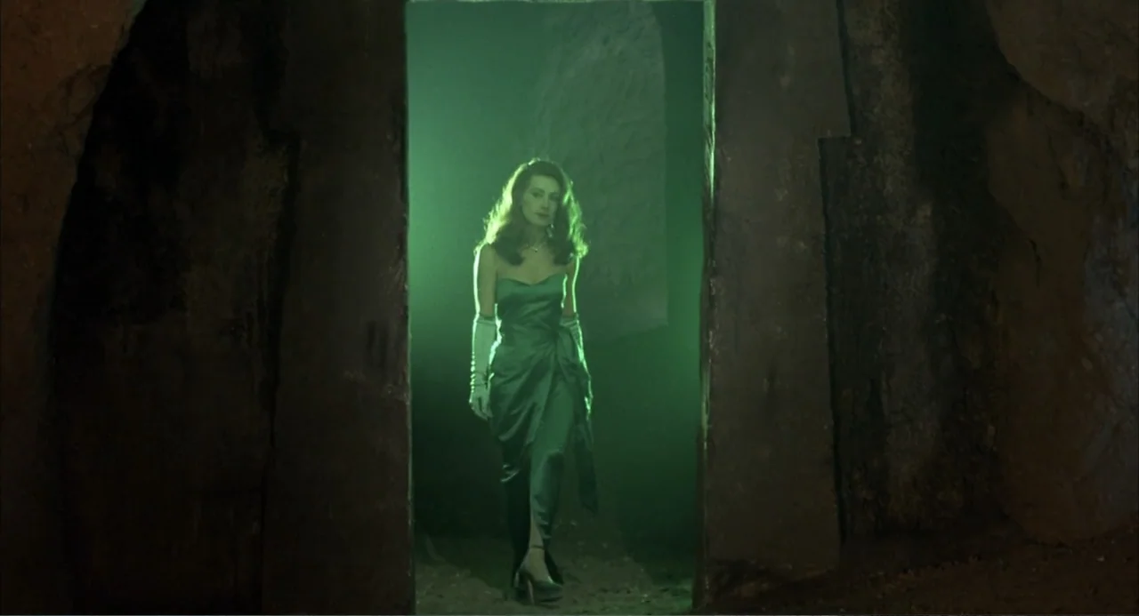 Zone Troopers (1985) movie still: fullbody — A woman stands in the threshold of a dark rocky cavern opening. The background is washed in a bright…