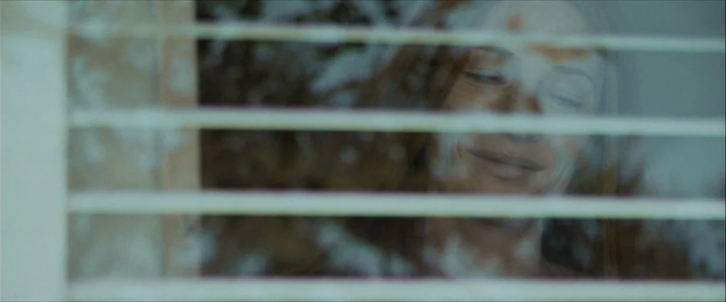 The Curious Case Of Benjamin Button (2008) movie still: closeup — A woman looks through the slats of white horizontal window blinds into a space.…