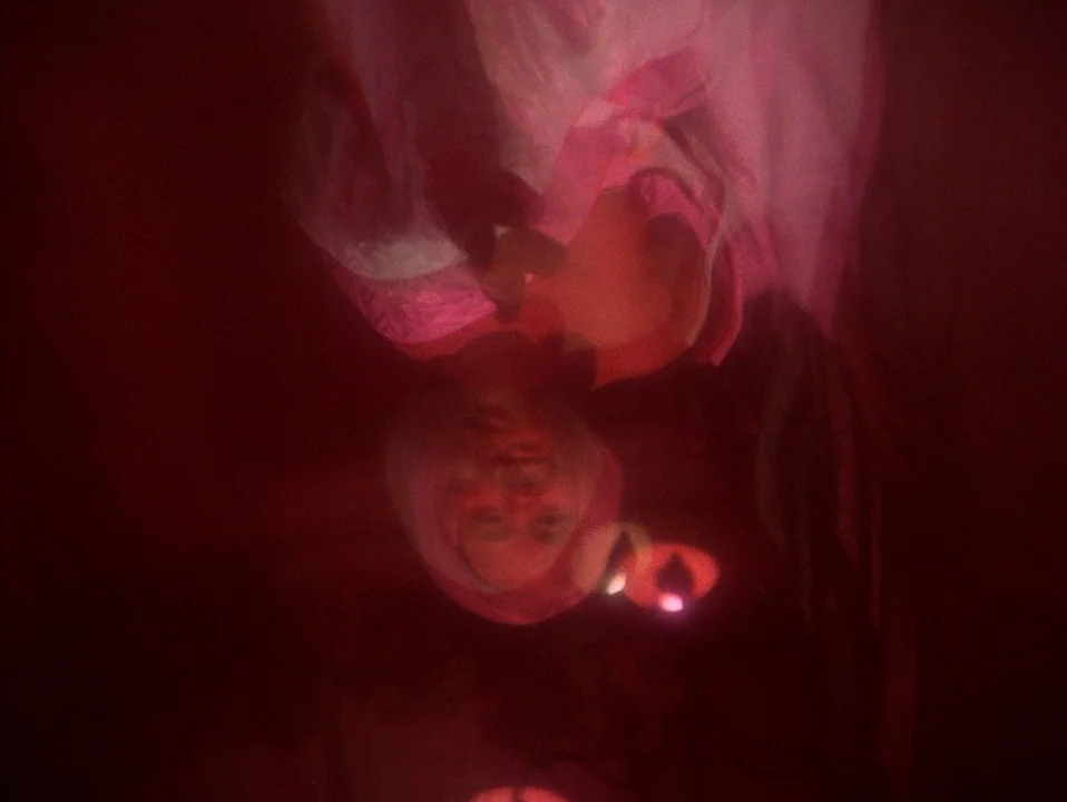 House (Hausu) (1977) movie still: closeup — A person hangs upside down in a dimly lit, red-saturated interior space. The subject's face is dimly…