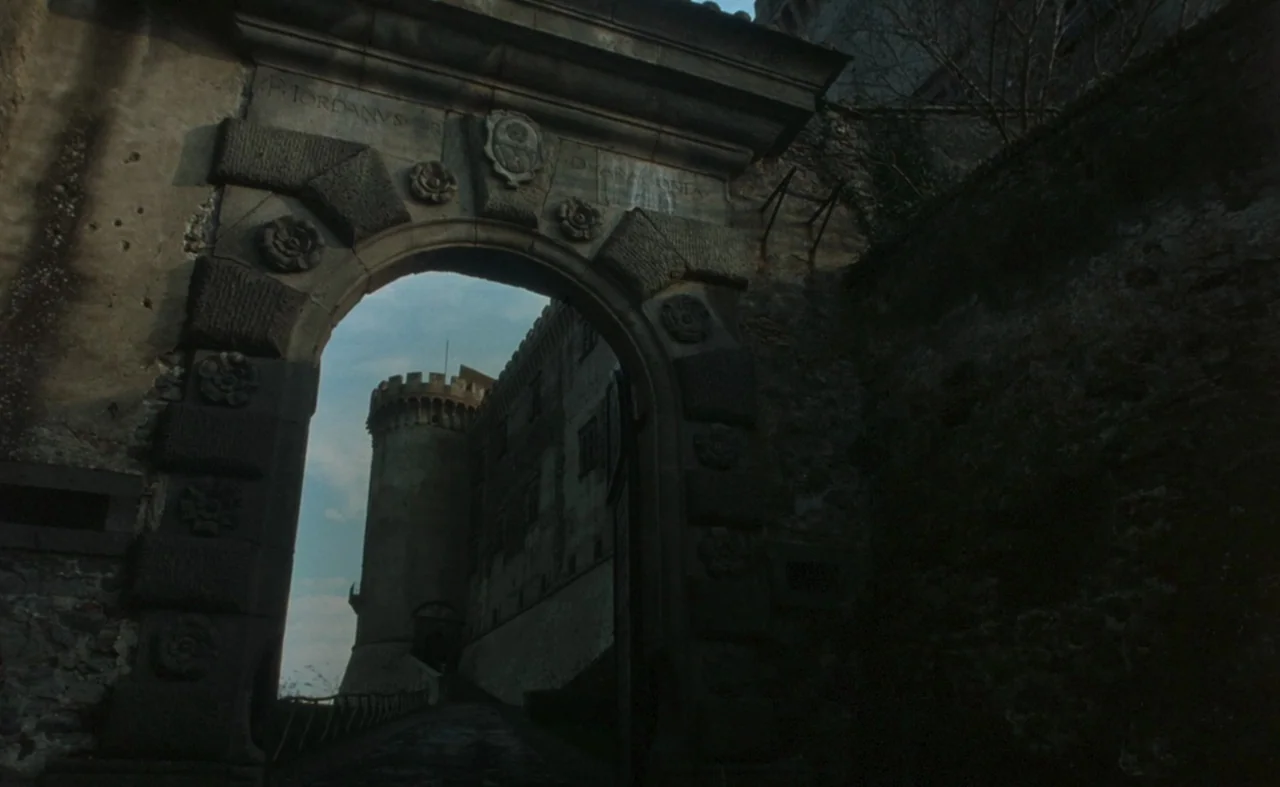 The Pit and The Pendulum (1991) movie still: establishing — A stone masonry archway serves as an entrance to a fortress with crenellated towers. The…